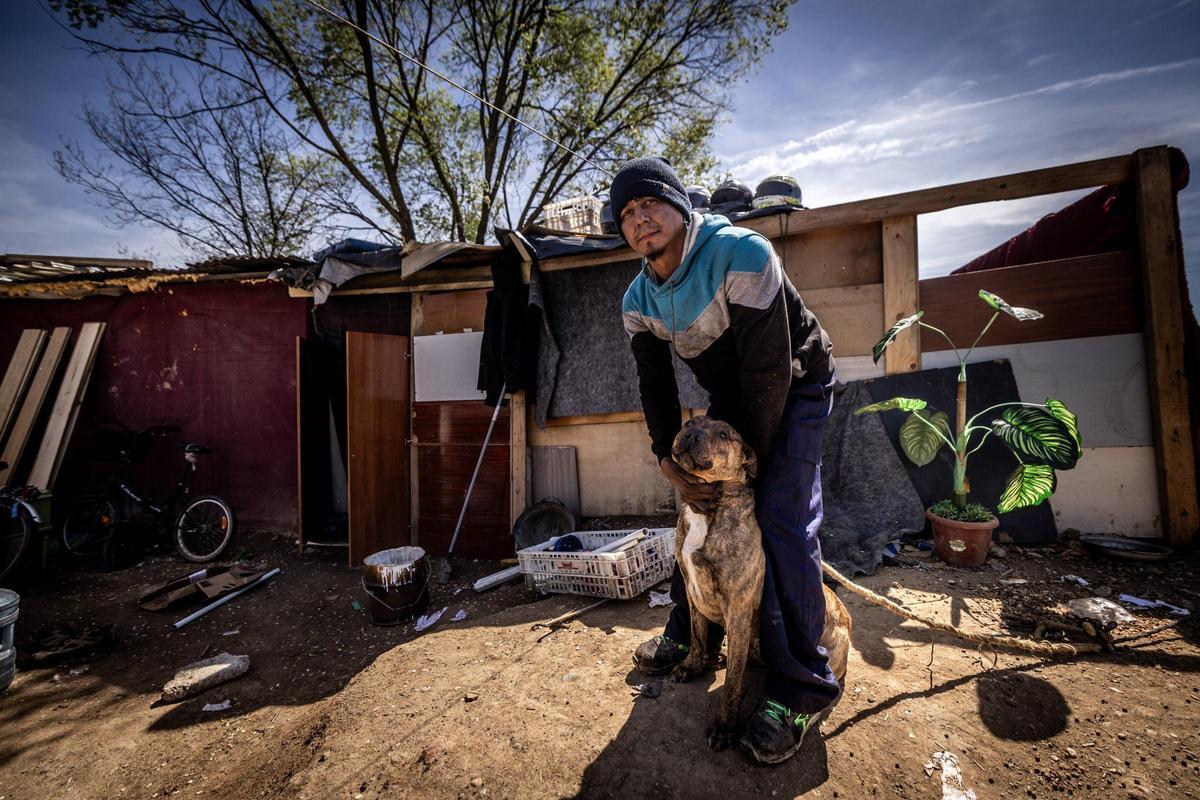 Carlos posa con su perro delante de la chabola donde viven.