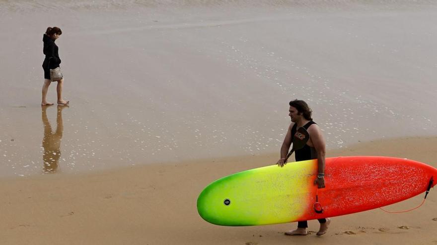 Una joven paseante y un surfero en la playa de San Lorenzo.