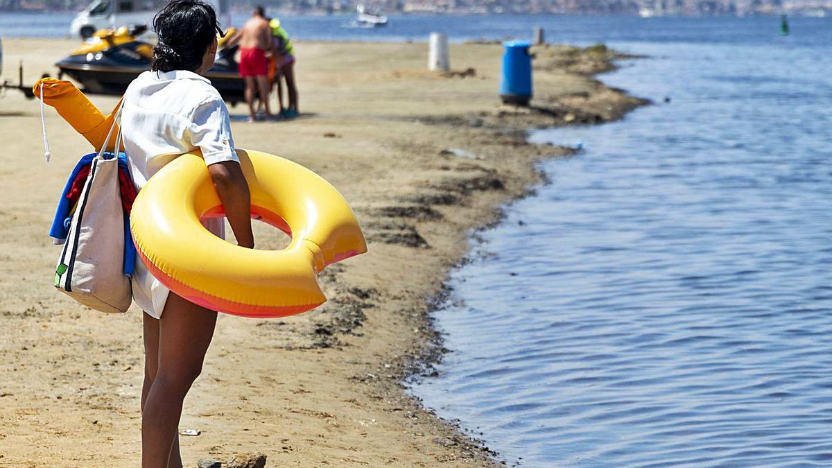 Una mujer cargada con enseres para pasar el día en la playa de Porto Bello, observa el Mar Menor. | IVÁN J. URQUÍZAR