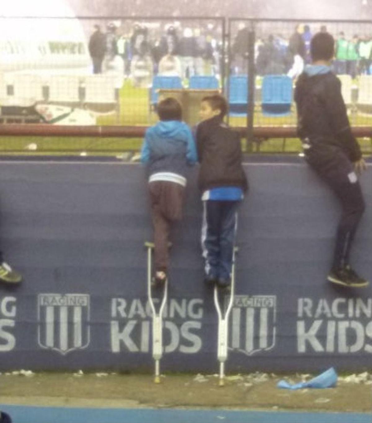 Santy y su amigo, encaramados en las muletas del primero para ver el partido del Racing Club Avellaneda, en Argentina.