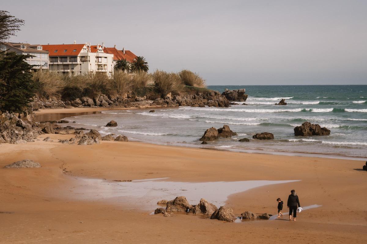 Una mujer pasea con un niño por la playa de Tregandin de Noja.