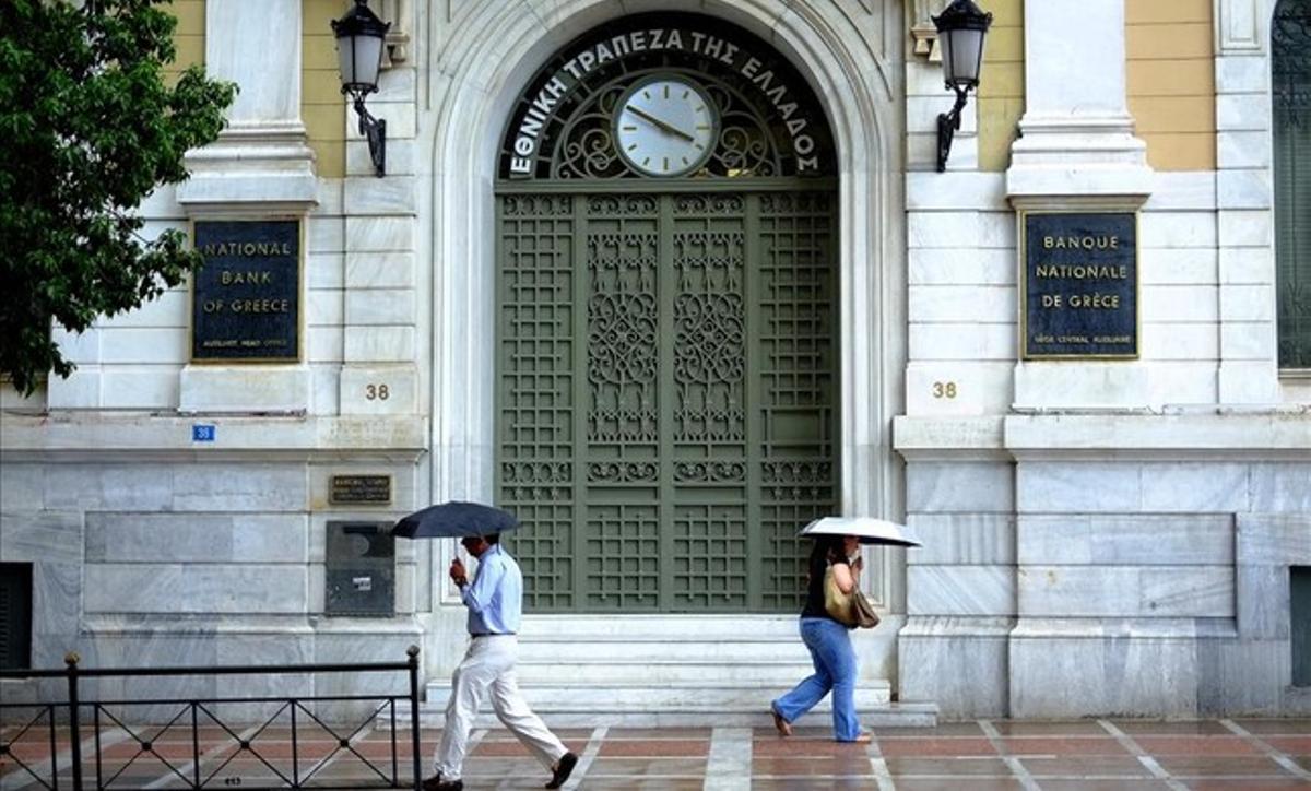 Dos ciudadanos pasan frente a una oficina del Banco Nacional de Grecia, en Atenas.
