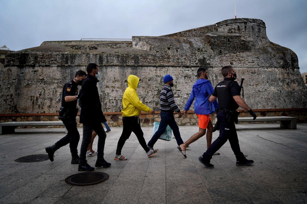 Un grupo de migrantes detenidos es conducido a un vehículo policial en el centro de Ceuta. Al fondo de la imagen, las murallas de la ciudad.