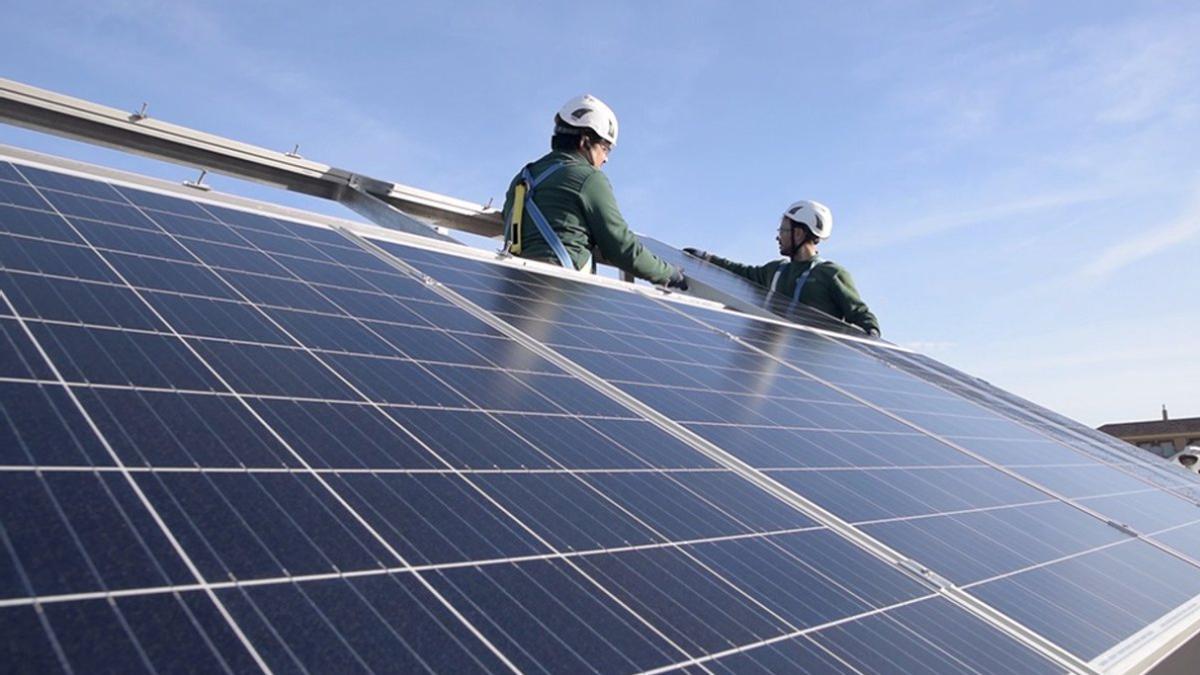 Dos operarios instalan placas fotovoltaicas en el tejado de una vivienda.