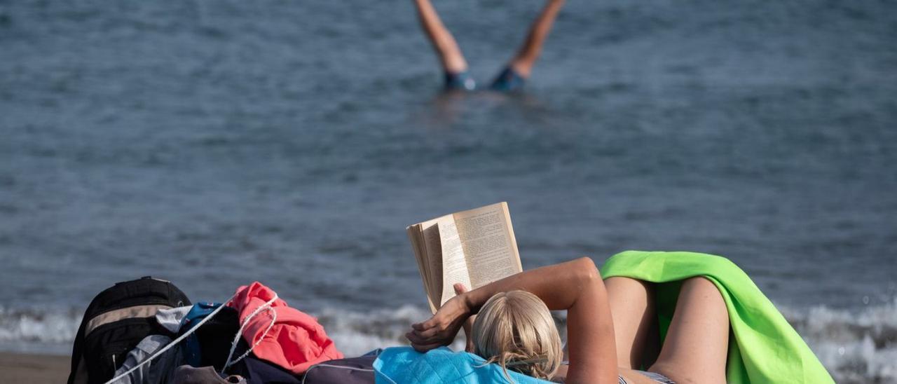 Una mujer se relaja en la playa leyendo un libro.  | | E.D.