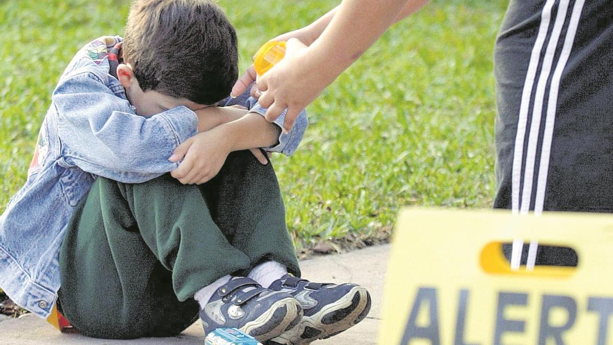 Un niño se cubre la cara mientras es asistido por su profesora