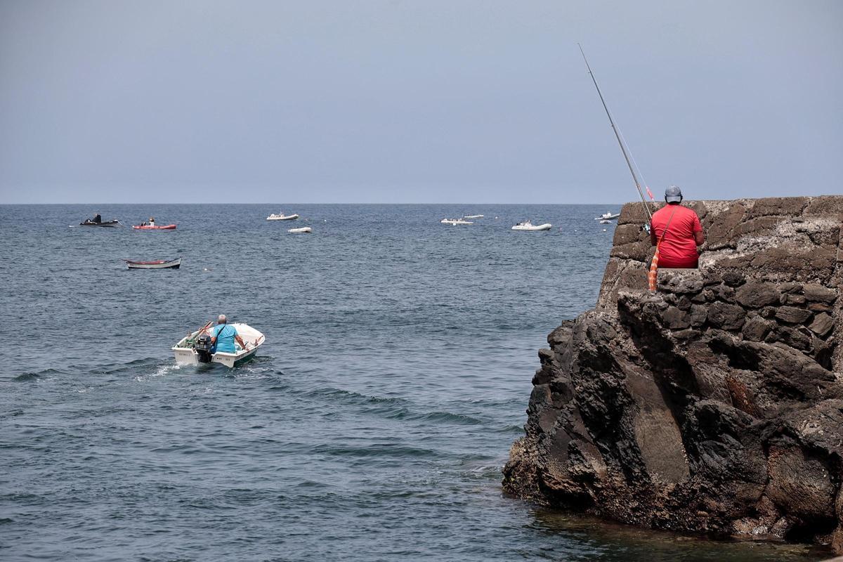 Un pescador con caña en mano y otro embarcándose en la costa de la punta