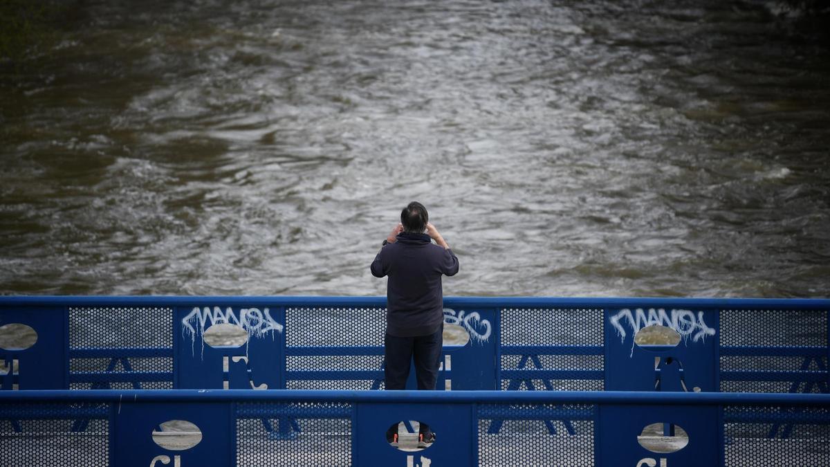 Una persona fotografía la crecida del río, en el parque lineal del Manzanares, a 20 de marzo de 2025, en Madrid (España).