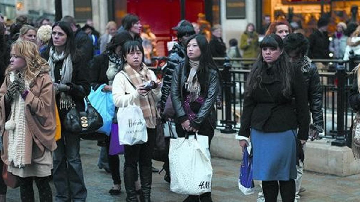 Consumismo a la baja 8 Unos londinenses, de compras navideñas en Oxford Street de Londres, esperan a cruzar la calle.