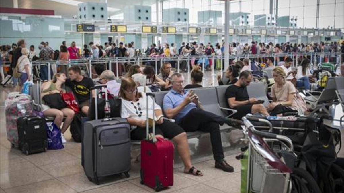 Colas frente al control de seguridad  y pasajeros esperando en las instalaciones del aeropuerto de El Prat, ayer.