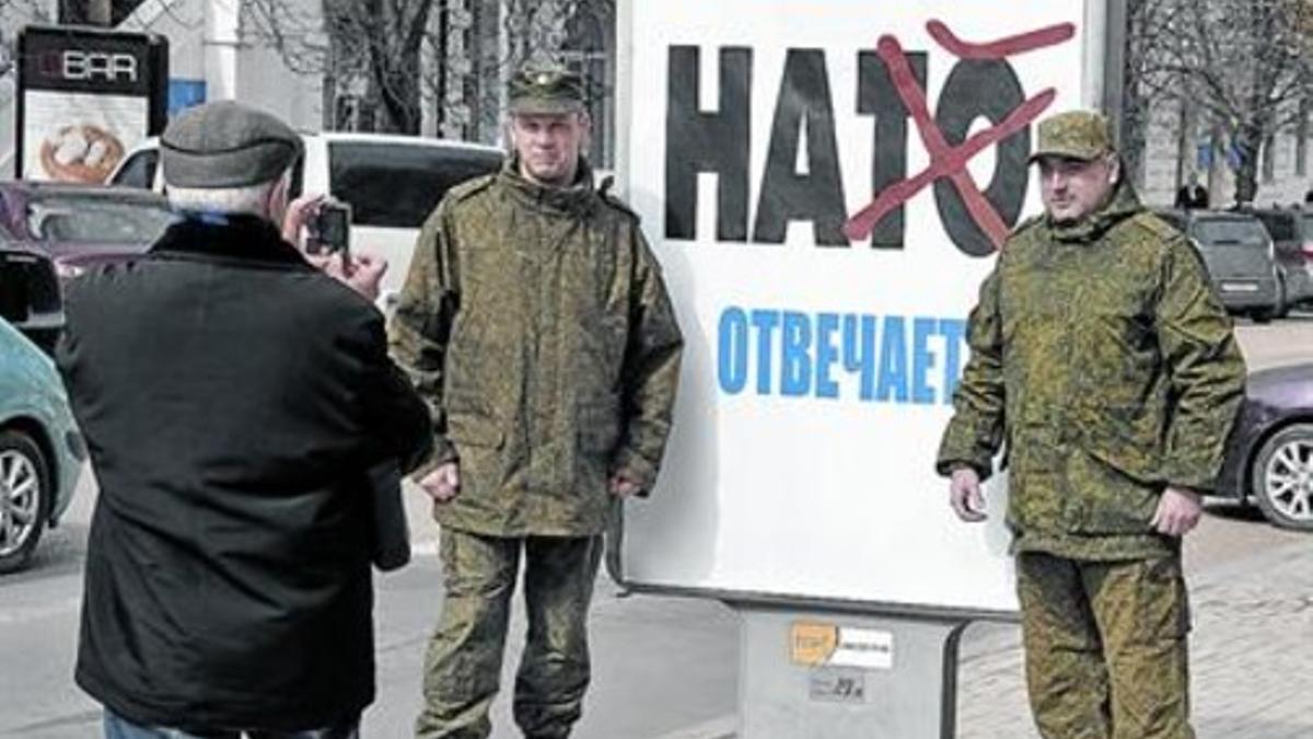 Militares rusos (sin insignias) junto a un cartel contra la OTAN en Crimea.