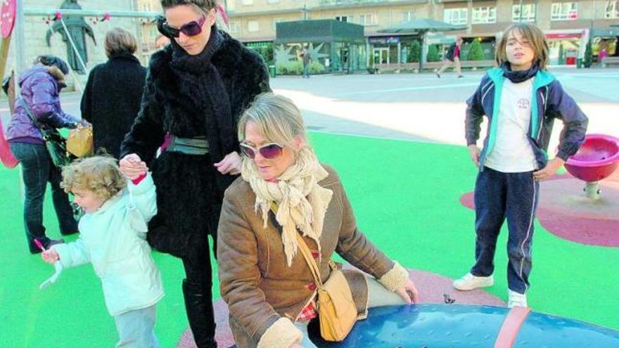 María Isabel de Nicolás, sentada, y Paola Nieto, en un parque infantil de Oviedo con unos niños.