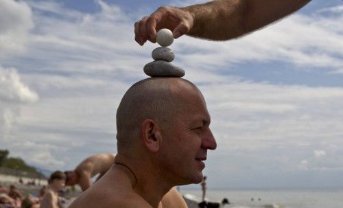 Engineer Yuri erects a stone pyramid on the head of his acquaintance and colleague Alexander as they rest on the beach in the Adler district of Sochi