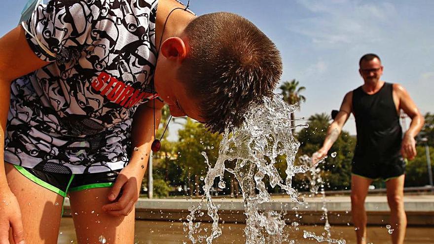 Un joven se refresca del calor en una fuente en el vial.