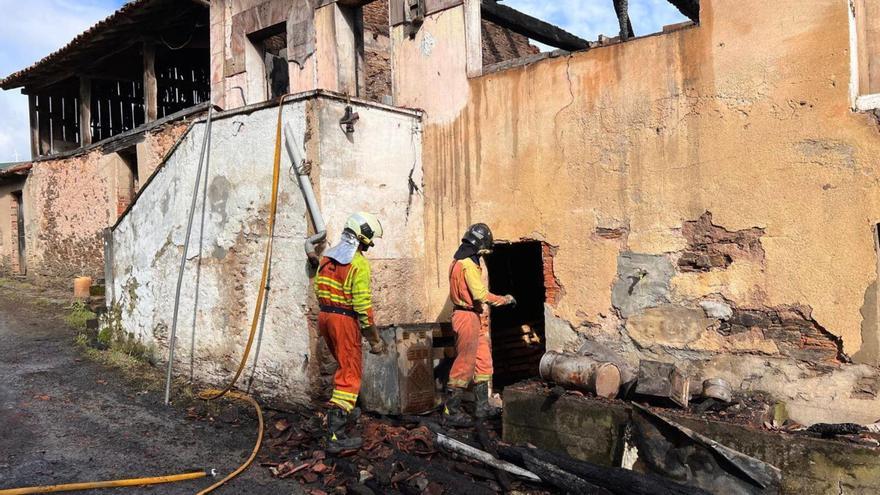 Dos bomberos del parque de Tineo inspeccionan los restos de la vivienda.