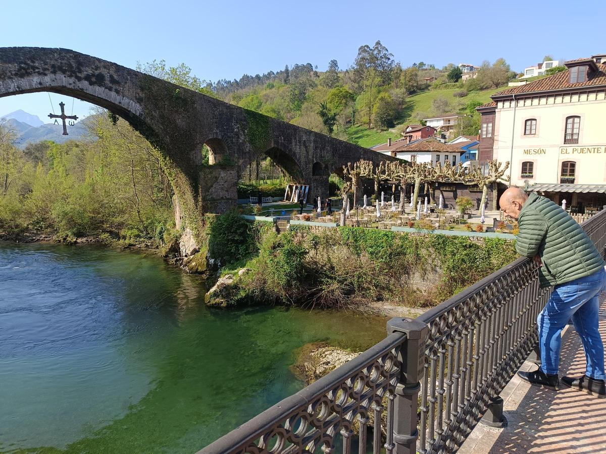Un vecino observa el estado del Sella junto al puente romano; al fondo, el lugar donde se subastará el campanu.