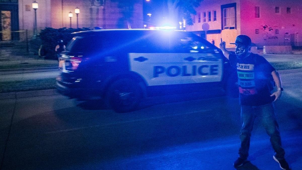 Un manifestante gesticula ante el paso de un vehículo de policía, la noche del miércoles en Kenosha.