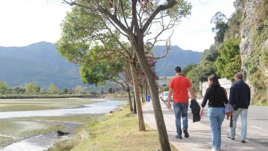 Peatones caminando por la avenida de Tito Bustillo, con la ría a la izquierda y la cueva a la derecha.