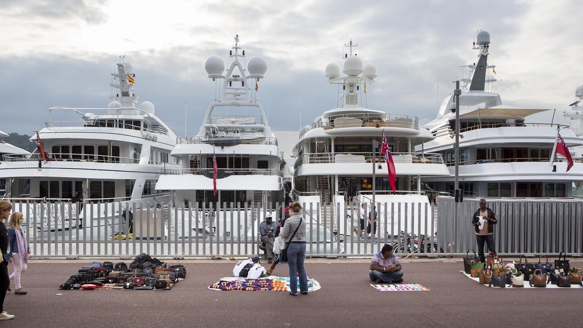 Barcos de lujo y manteros en el Port Vell de Barcelona.