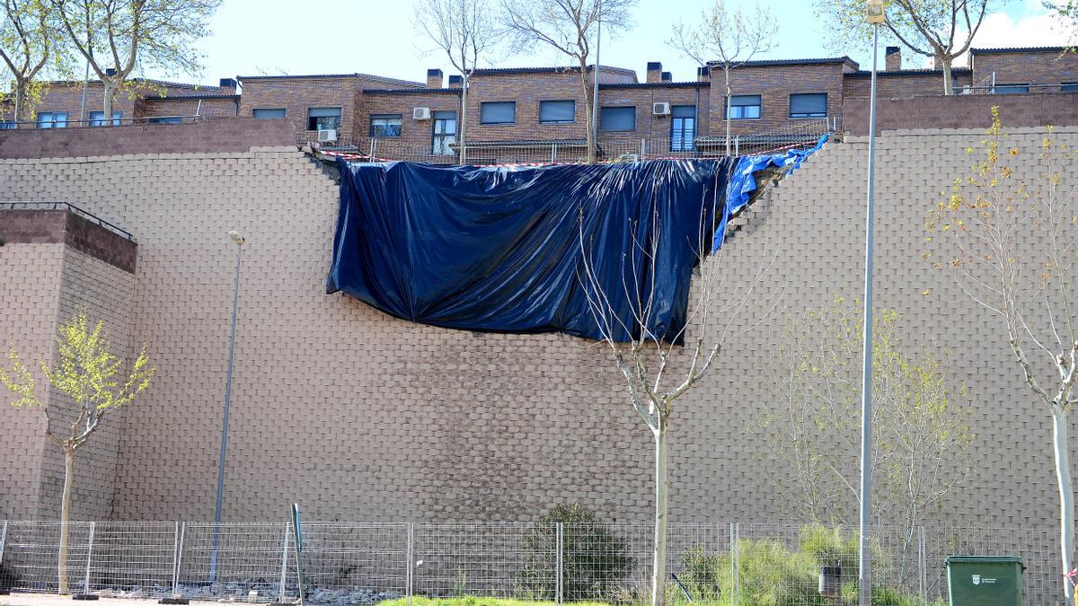 Valla en la acera, con los escombros y plástico que tapa la zona del muro que se derrumbó en Plasencia.