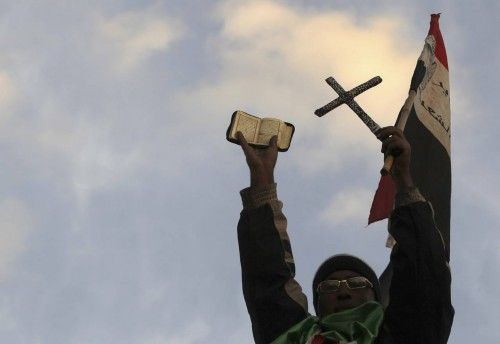 An anti-Mursi protester holds the Koran, a Cross and the Egyptian national flag on top of a wall in front of the presidential palace in Cairo