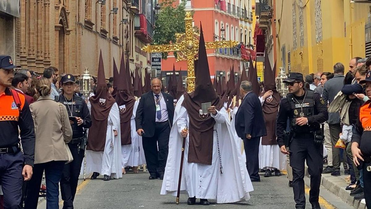 La cruz de guía del Carmen Doloroso avanza por la calle Trajano a las altura de los Luises con los tramos de a tres. De fondo se oye la banda del misterio.