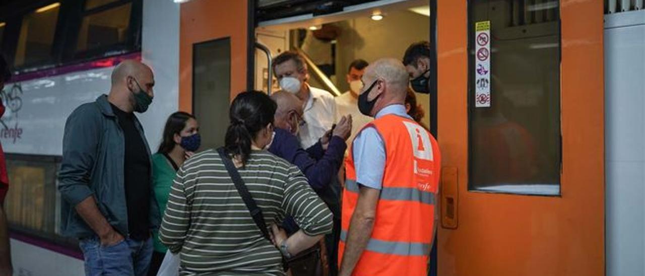 Pasajeros y un informador de Rodalies junto a un tren, en la estación de Sants.