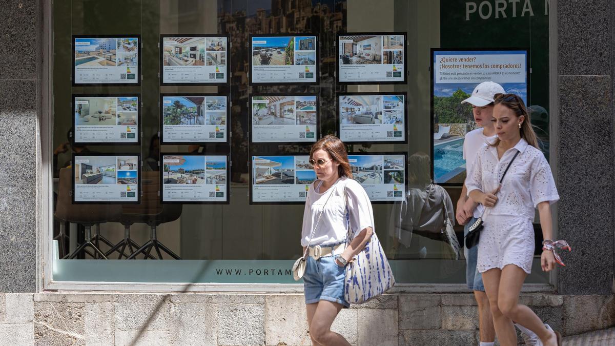 Archivo - Varias personas pasan junto a los anuncios de viviendas en venta en una inmobiliaria.