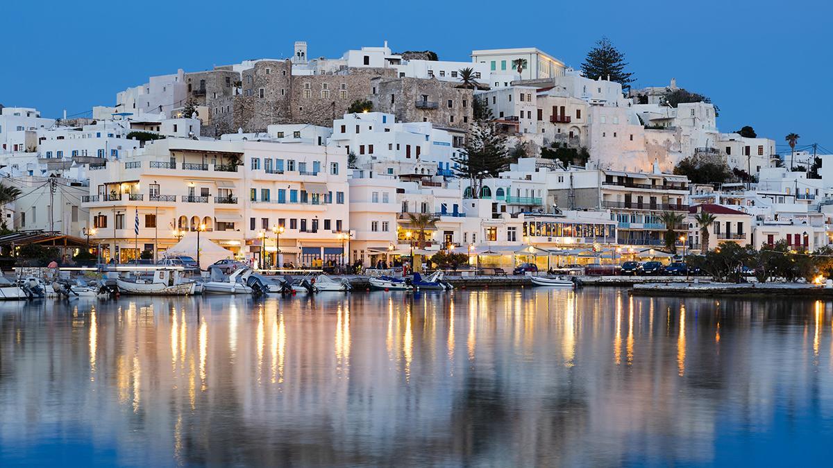 Naxos conserva un ritmo más local, con su puerto iluminado y el casco antiguo extendiéndose hacia la colina.