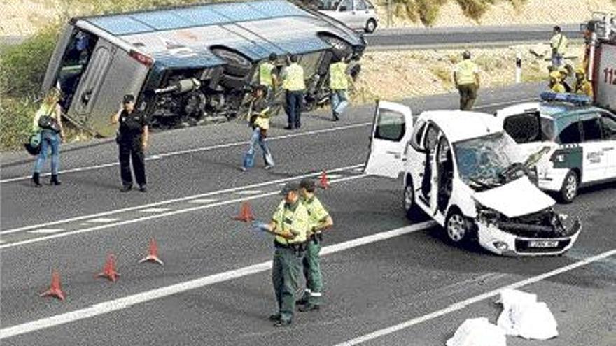 Los dos fallecidos en Elx junto al vehículo siniestrado y, al fondo, el autobús volcado.