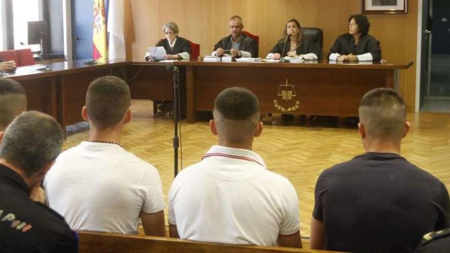 Los cuatro acusados, de espaldas y custodiados por policías, en el juicio ayer en Vigo. // Marcos Canosa