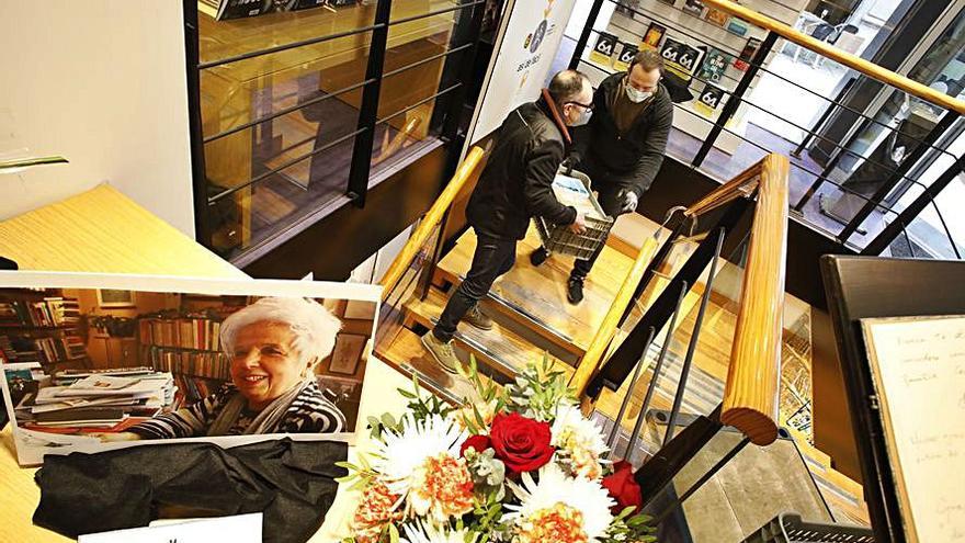 Dos empleados subiendo cargando libros en Cervantes, con una fotografía en recuerdo a Conchita Quirós en primer plano. |Ángel González