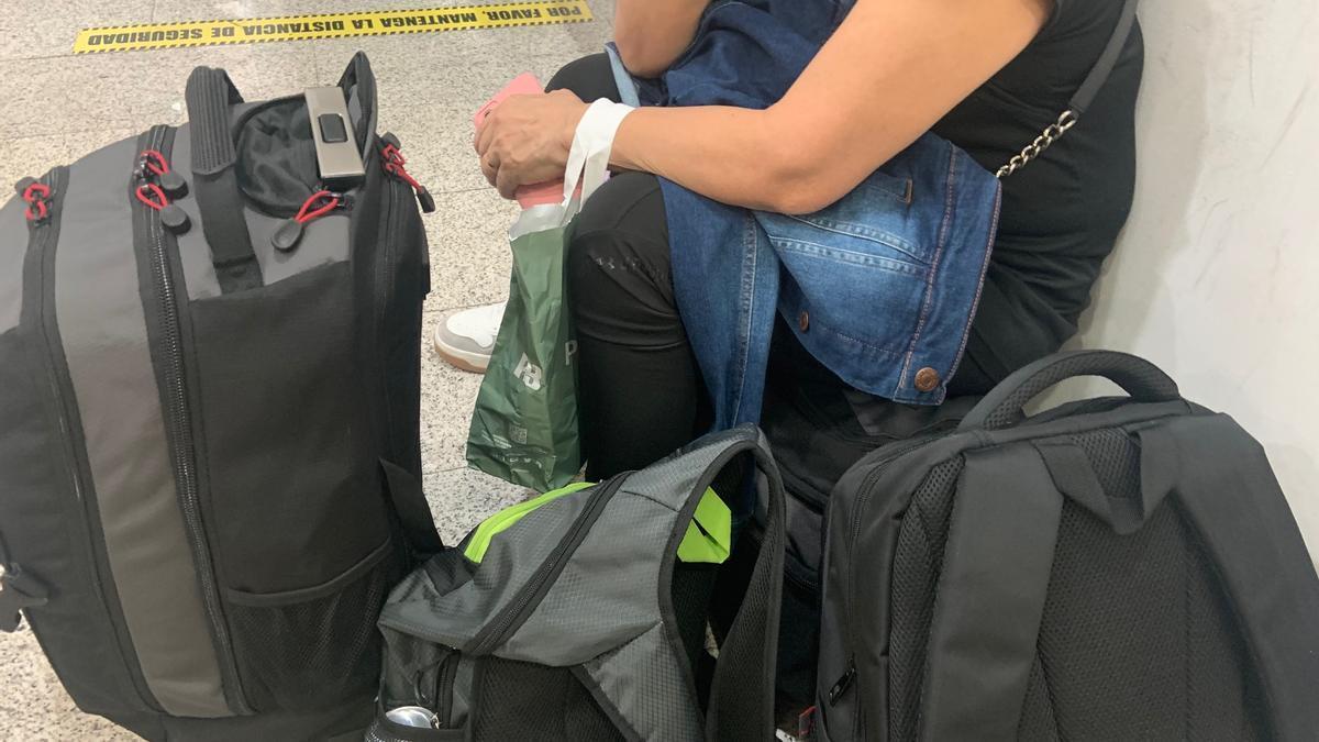 Silvia M. sentada sobre sus maletas, espera la devolución del billete.