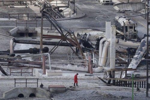A man walks near burnt vehicles and gas storage tanks at a gas facility of Pemex in Reynosa