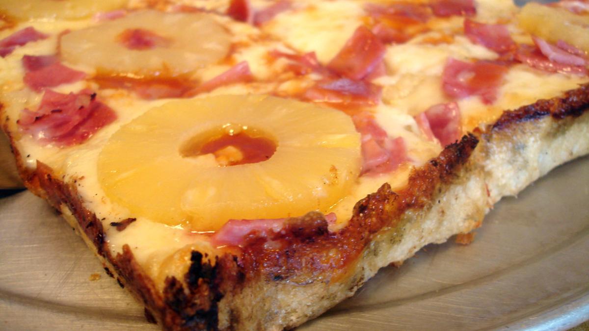 Una porción de pizza hawaiana, con rodajas de piña enteras.