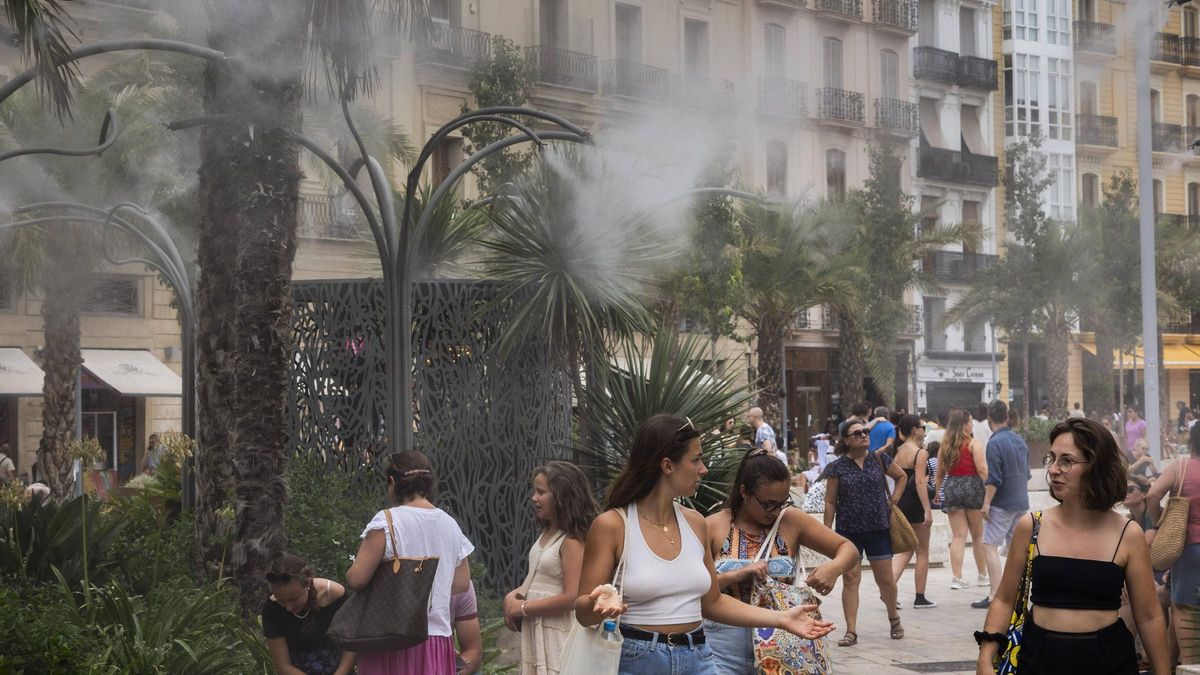 Viandantes se refrescan bajo los aspersores de la plaza de la Reina de València.