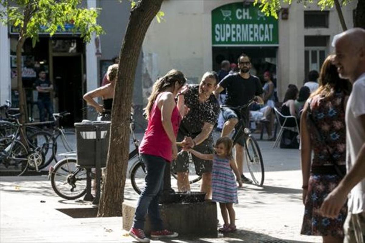 Uns vianants es refresquen en una font de la plaça d’Osca de Barcelona, dissabte passat.