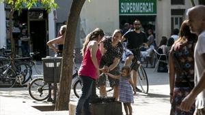 Uns vianants es refresquen en una font de la plaça d’Osca de Barcelona, dissabte passat.