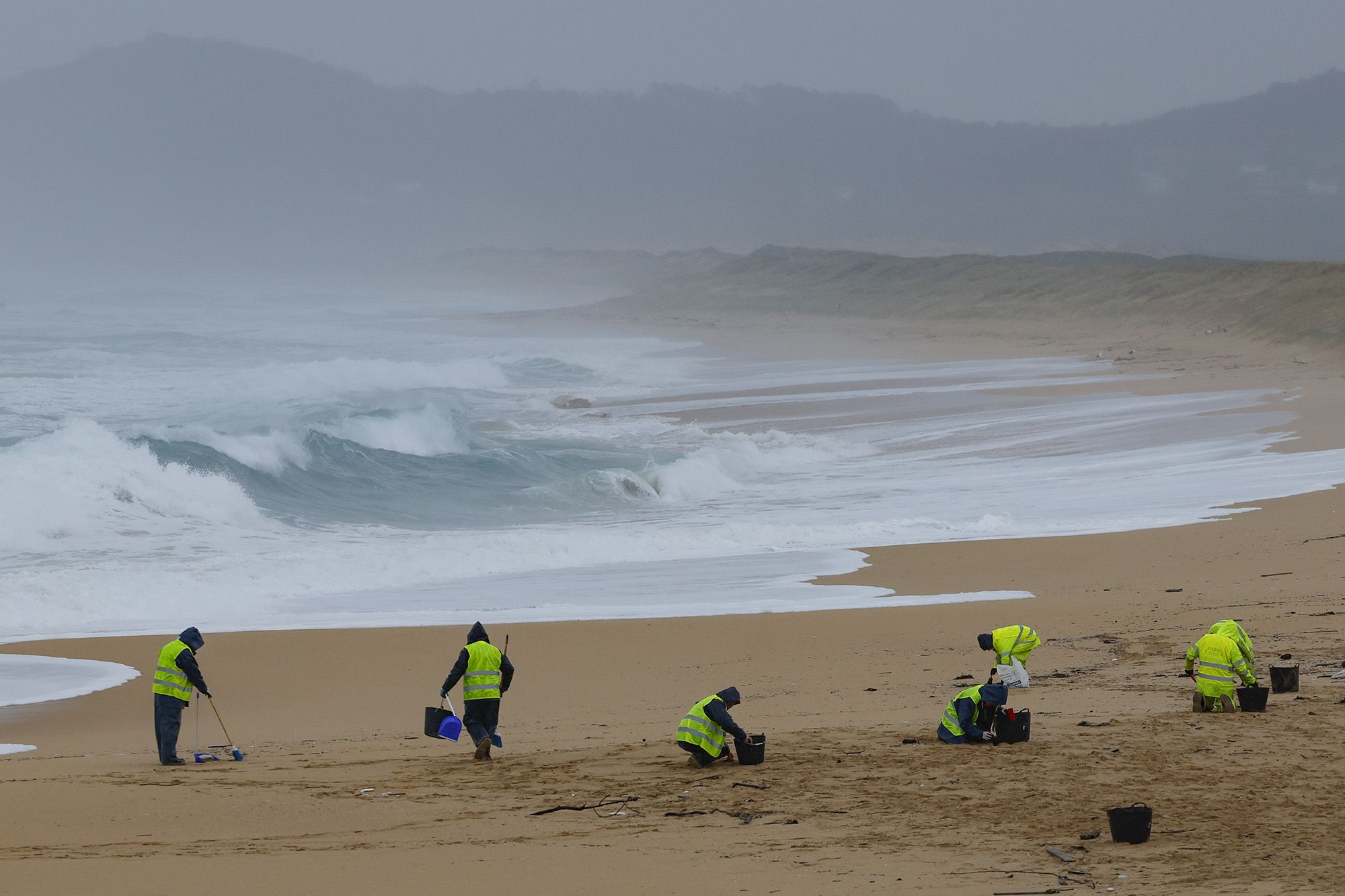 Operarios limpiando pellets de plástico en el parque natural de Corrubedo