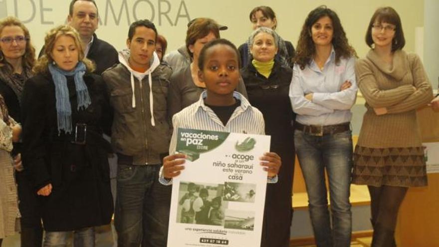El joven saharaui Ahmed Masud sostiene el cartel promocional del programa «Vacaciones en paz».