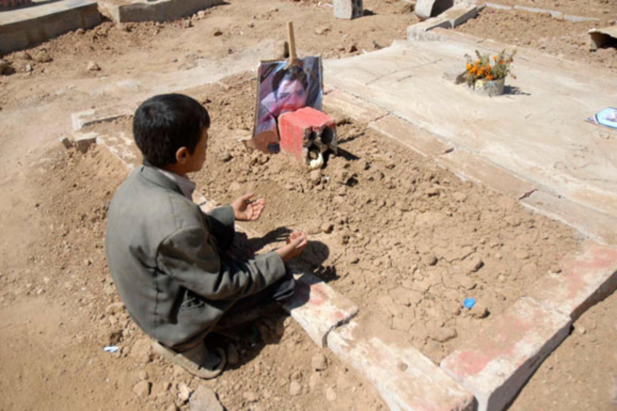 Un nen s’asseu al costat de la tomba del seu germà durant el funeral de 12 manifestants a Sanà (Iemen).