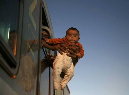 Migrant holds baby outside window of train while waiting to depart from station in Tovarnik
