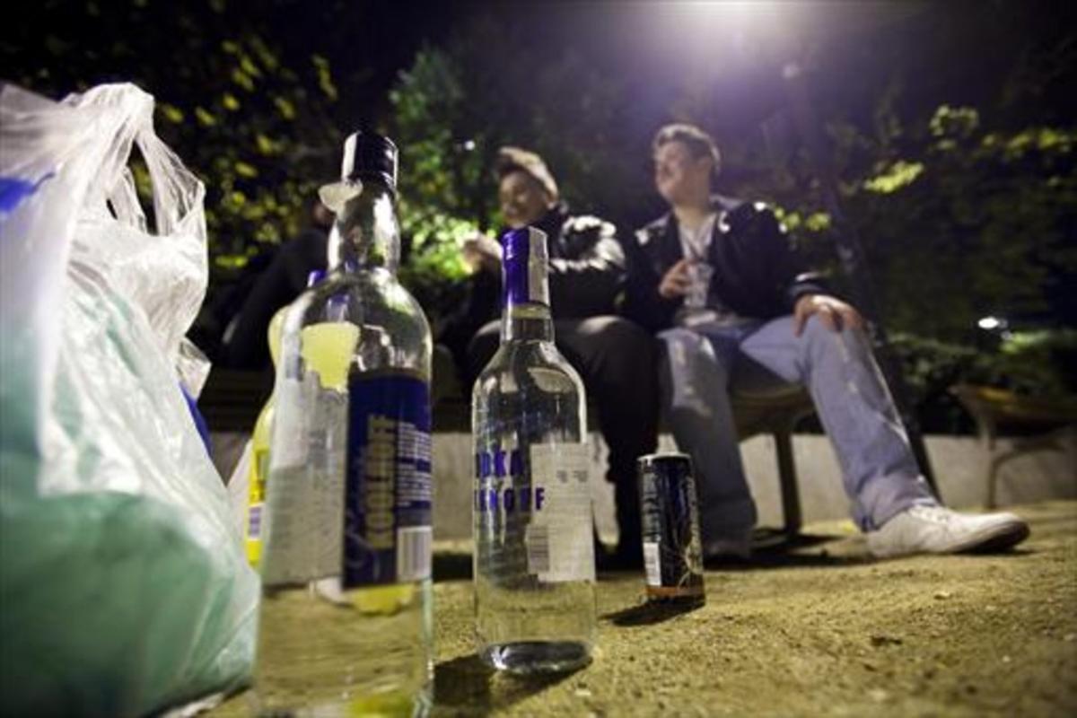Dos jóvenes beben en un banco público durante un botellón nocturno montado, con alcohol de alta graduación, en la plaza de Letamendi del Eixample de Barcelona.