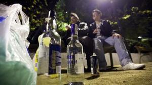 Dos jóvenes beben en un banco público durante un botellón nocturno montado, con alcohol de alta graduación, en la plaza de Letamendi del Eixample de Barcelona.