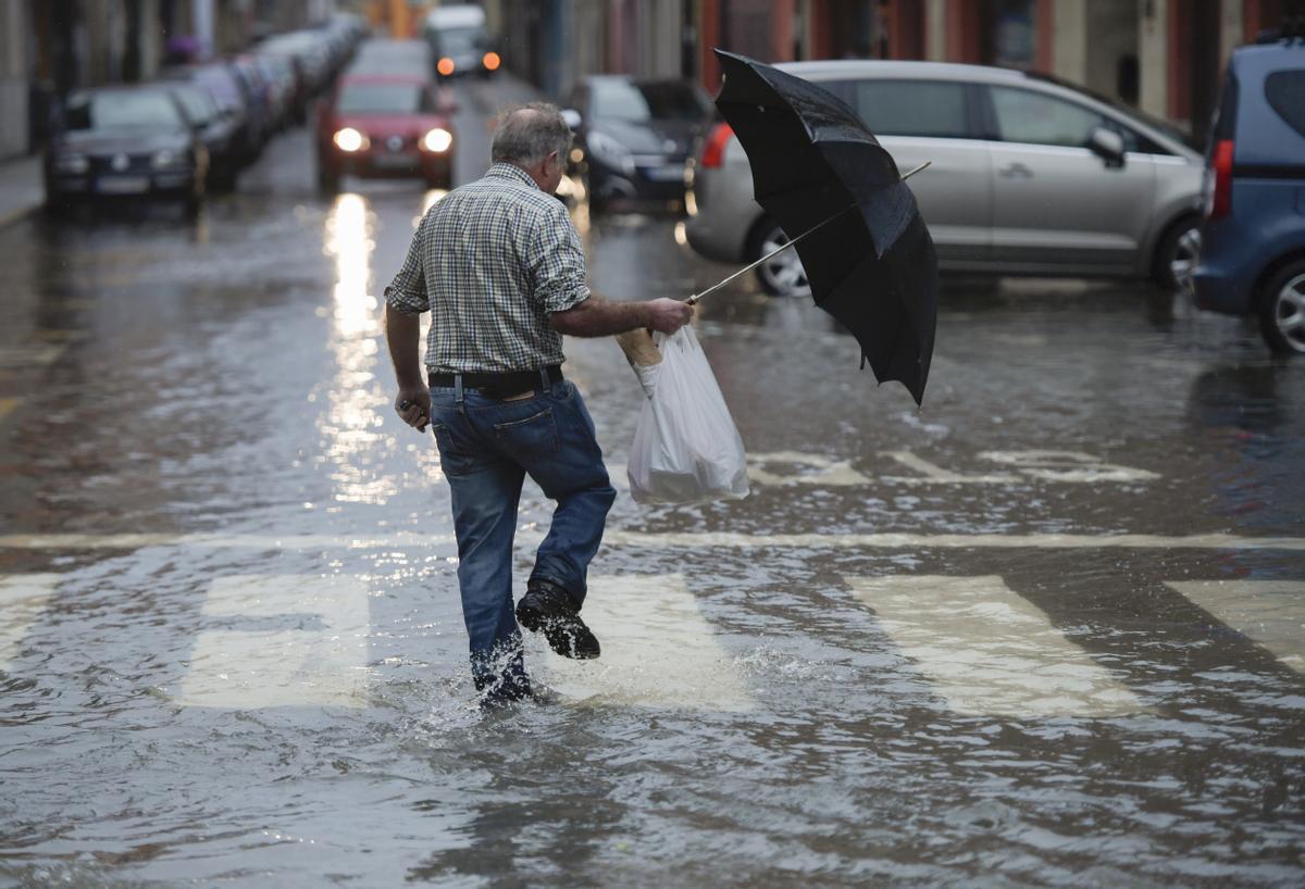 Un hombre camina por una de las inundadas calles de Villaviciosa este mediodía. En Asturias, el nivel de los ríos Narcea, Linares y Cares ha descendido, tras encontrarse en nivel prealerta esta mañana por las intensas lluvias caídas desde este lunes, pero ha obligado a suspender las clases en tres centros educativos.