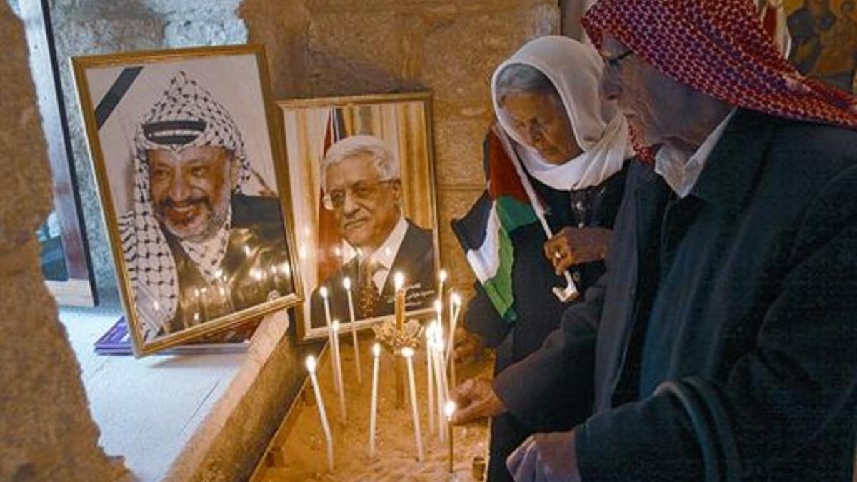 Dos palestinos ponen velas junto a las fotografías de Yaser Arafat y Mahmud Abbás, ayer en Cisjordania.