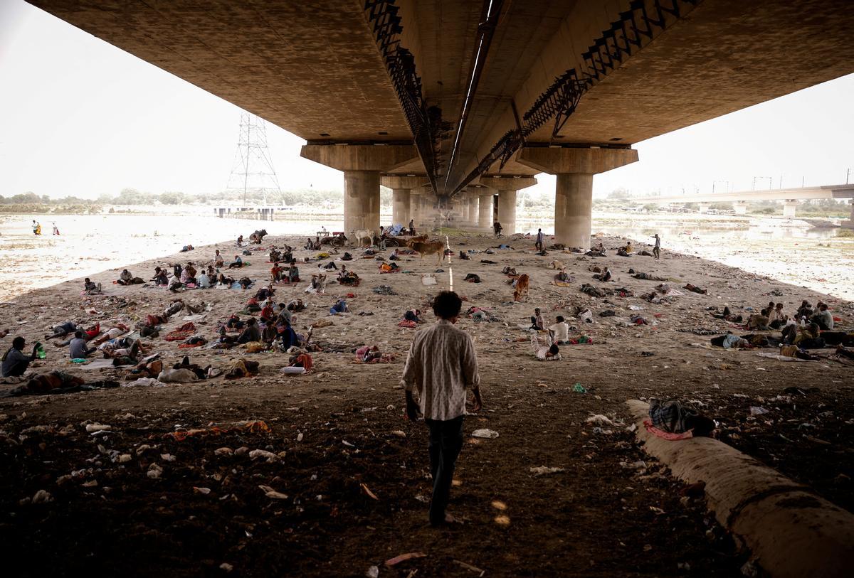 Un numeroso grupo de gente duerme en el lecho del río Yamuna, en Nueva Delhi, a la sombra que les proporciona un puente.