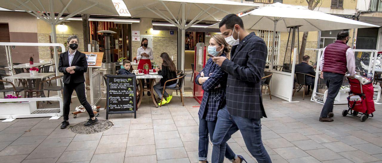 Ciudadanos con mascarilla pasando por una terraza en Palma