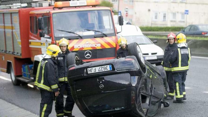 Bomberos, junto al coche volcado ayer en la avenida Alfonso Molina.