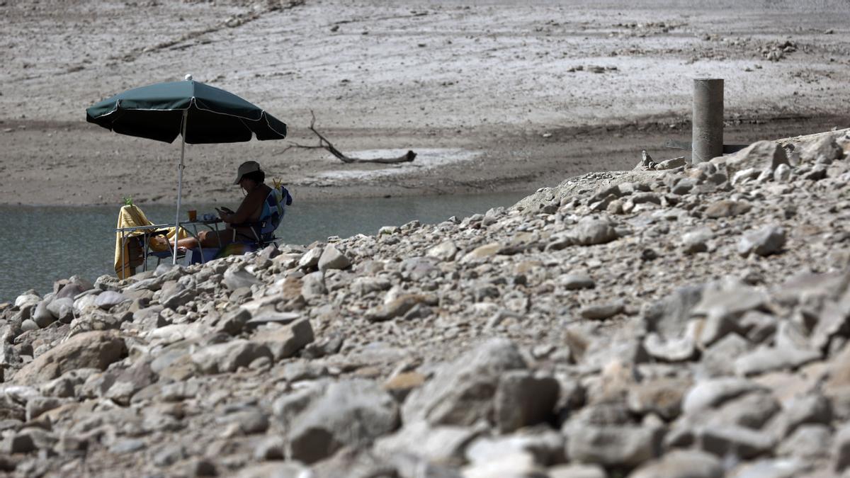  Una persona se protege del sol con una sombrilla en el pantano de Yesa donde se aprecia ya la bajada de la cota de agua